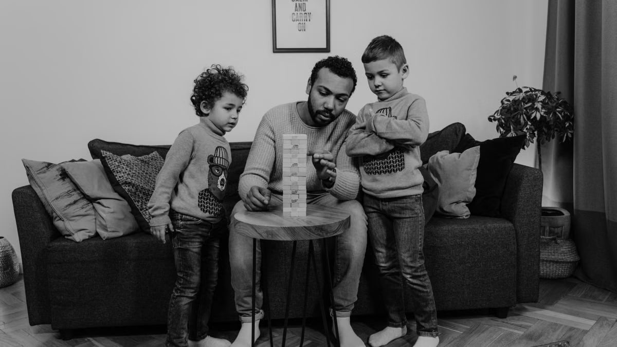 Father and sons enjoy quality time indoors building a wooden tower on the sofa.